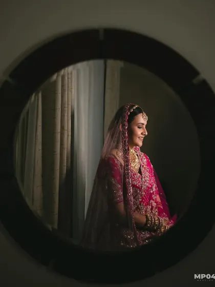 A creative shot of my bride Aayushii, captured through a mirror. The lighting is soft and highlights her serene expression and beautiful makeup.