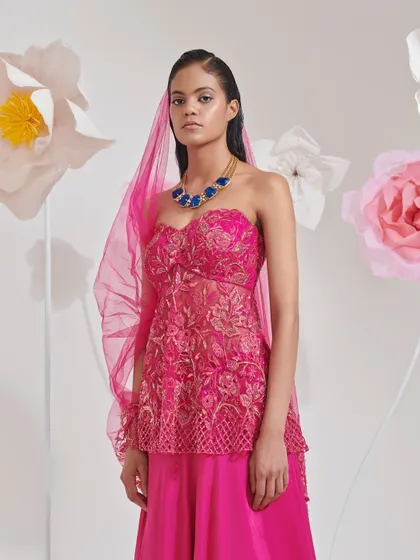 A strapless peplum top in bright pink paired with a matching skirt and a sheer veil. This is a modern and youthful look for a pre-wedding event.
