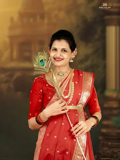 A beautiful solo portrait celebrating tradition. The mother-to-be is dressed in a stunning red saree, holding a peacock feather, which adds a touch of divine symbolism to the maternity photo.