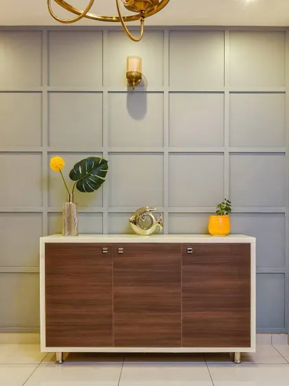 A stylish console cabinet with a dark wood finish and a white frame. It is set against a grey wall with decorative beading, creating an elegant focal point in a foyer or dining area.