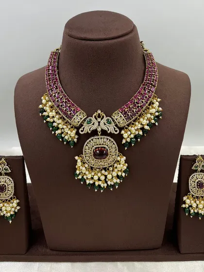 This antique-finish necklace set features peacock motifs and intricate ruby and green stone work. It comes with matching earrings and is perfect for customers who appreciate detailed, traditional designs.