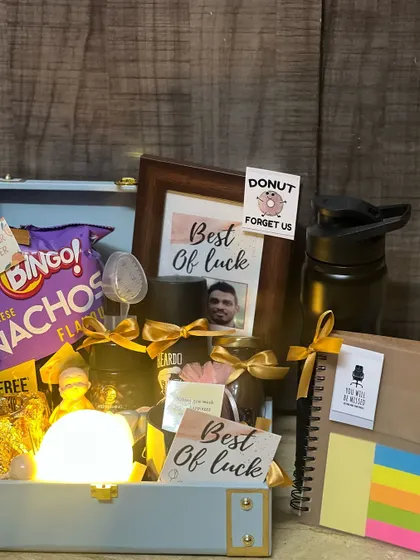 This farewell hamper includes a personalized photo frame, making it a truly special keepsake. It's combined with practical items like a notebook and fun items like snacks.