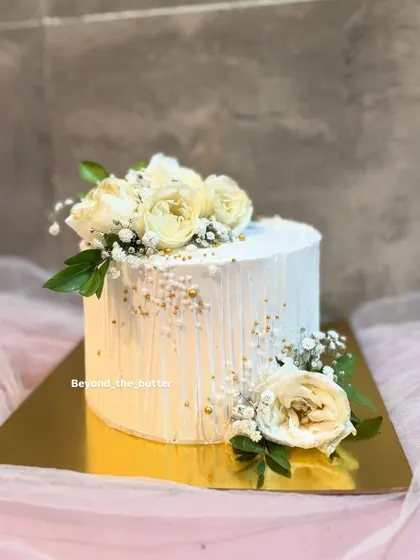 A closer look at this minimalist white cake, highlighting the delicate vertical texture of the buttercream and the simple, elegant arrangement of fresh white roses.