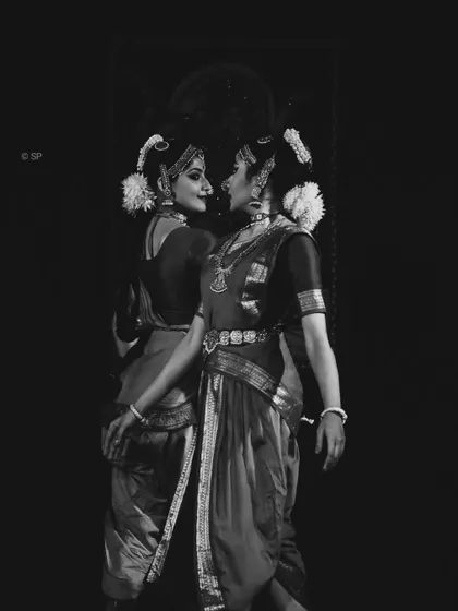 A black and white shot capturing an intimate moment of connection in the Ardhanareeshwara duet. The lighting emphasizes the forms and expressions of the dancers.