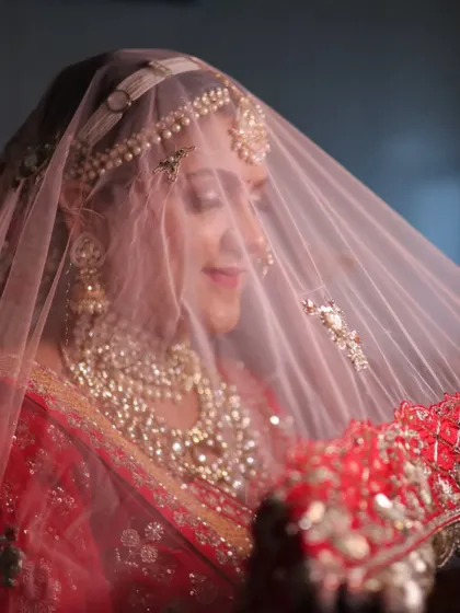 The classic bridal veil shot. The soft net veil adds a layer of mystique, while her glowing makeup and stunning jewelry peek through, creating a truly magical and timeless portrait.