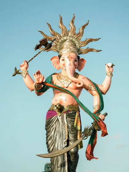A clear, full length shot of the majestic Mumbaicha Raja idol against a bright blue sky, highlighting its impressive craftsmanship and powerful stance.