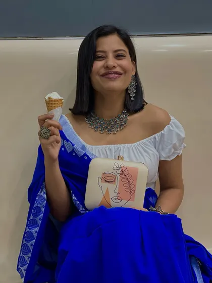 A full view of this chic and joyful ensemble. The clutch is held front and center, showing off its unique design while the customer enjoys a sweet treat. It's all about finding style in everyday moments.