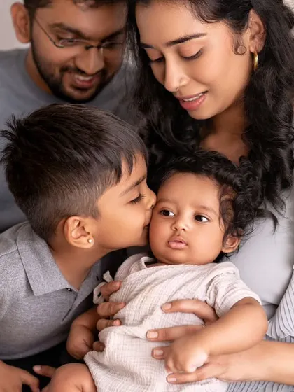 A beautiful family of four, with the older brother giving his new baby sibling a gentle kiss. A perfect portrait of growing love.