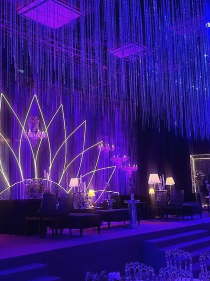 A view of the main stage and lounge area, showing the interplay of the neon lotus, crystal curtains, and sophisticated dark furniture. The design is a perfect example of modern luxury for a sangeet celebration.