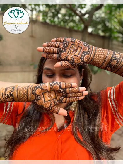 A happy bride showing off her full bridal mehendi, which features traditional square patterns and floral motifs.