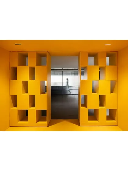 A sculptural, bright yellow partition wall at 'The Amber Encase' clubhouse. The wall's geometric cutouts create playful openings and visual interest, serving as both a functional space divider and a piece of installation art.