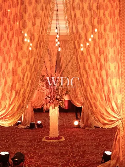 A grand entrance for a wedding at the Taj. The walkway is draped in patterned orange fabric, with a large floral centerpiece welcoming guests into the celebration.