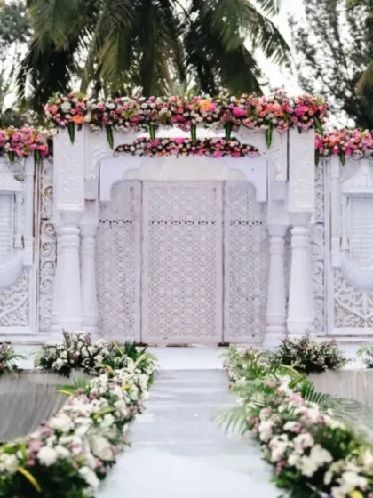 An ethereal wedding entrance designed to look like a pristine white temple gate, adorned with delicate pink and white florals. I create settings that feel like they are straight out of a fairytale.