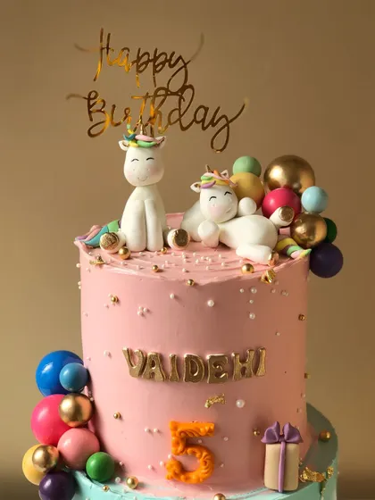 A close-up of a unicorn and dinosaur themed cake for twins, showing the adorable unicorn topper with colorful presents.