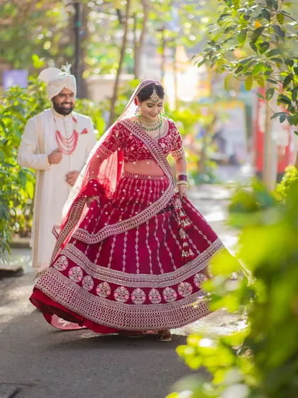 A candid shot of a bride in her red lehenga, twirling as her groom follows, captured in beautiful natural light.