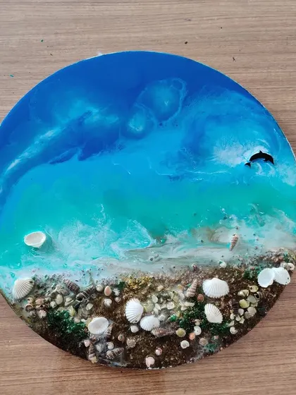 This finished resin piece captures the beauty of the sea, with swirling blue water and a textured, shell-strewn beach.