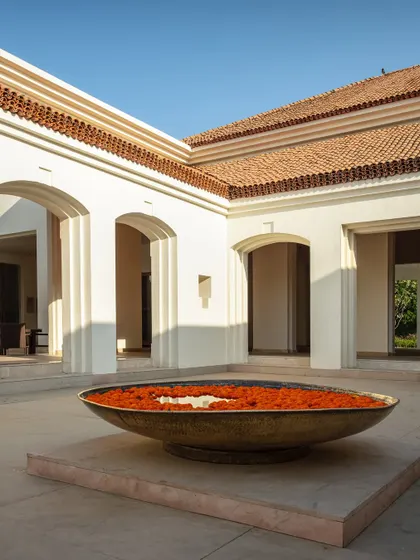 A central courtyard offers a moment of profound peace and welcome. The traditional brass 'urli' filled with flowers, set against the clean lines of modern arches, symbolizes our approach: a seamless blend of timeless Indian heritage and contemporary architectural thought.