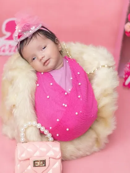 An awake newborn in a fun, pink Barbie-themed setup.