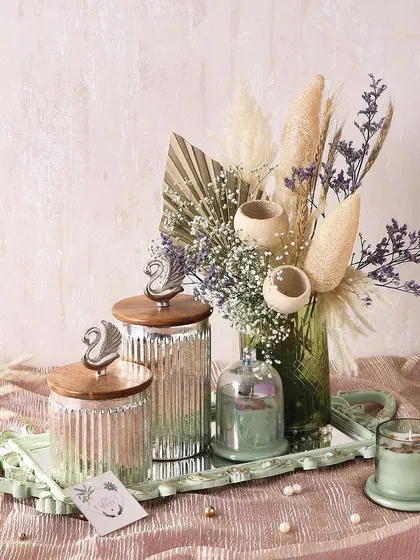 The Swan Hamper is designed for a sophisticated Diwali gift. It includes a candle, a mirror tray, a set of two swan jars filled with treats, and a beautiful flower arrangement.