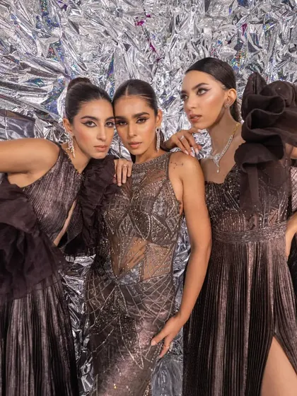 Three models styled in glamorous, textured gowns for a Kalki Fashion campaign. The metallic color palette and the shimmering background create a high-impact, futuristic look perfect for a cocktail or reception edit.