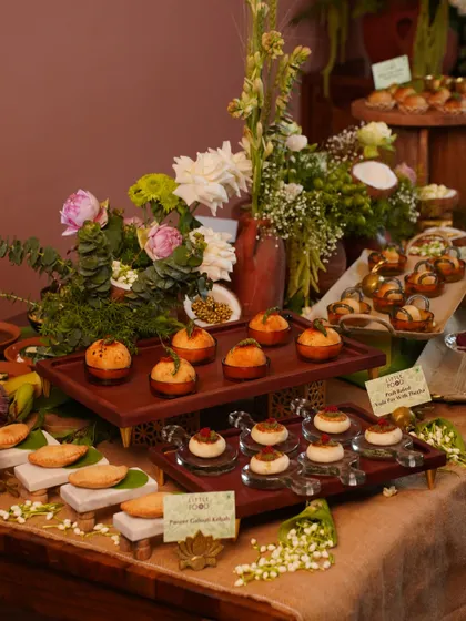 A beautifully tiered setup showcasing a variety of our bespoke Indian appetizers. This arrangement allows guests to easily see and select from different bites, like the Paneer Galouti Kebabs and Potli Samosas, amidst fresh floral decor.