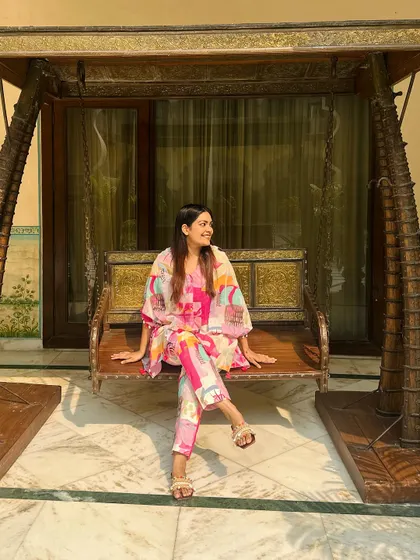Sitting on a traditional Indian swing, the bright pinks and oranges of my co-ord set pop against the heritage background.