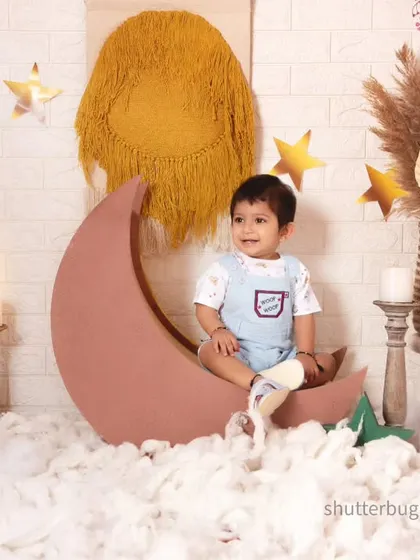 A happy boy sitting on a crescent moon prop in our dreamy and whimsical boho night-sky setup.