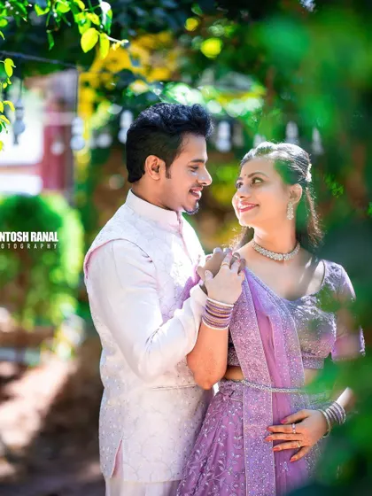 A soft and romantic portrait of a couple in light-colored traditional wear, framed by foliage.