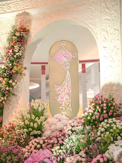 A detail of the floral decor, showing how beds of pink, white, and purple flowers frame a custom-designed panel featuring a stylized peacock. This element adds a layer of bespoke artistry to the event.