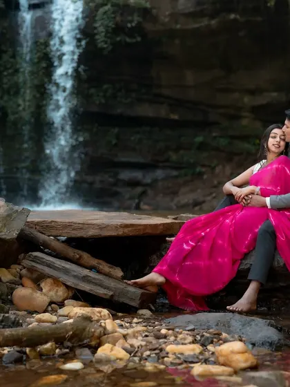 A romantic portrait of a couple sitting by a waterfall, wrapped in the bride's flowing pink saree. We use the natural environment to frame intimate and artistic pre-wedding shots.