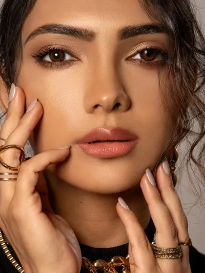 A soft and intimate beauty portrait. The styling is minimal to draw attention to the model's features and the delicate gold rings, creating a natural and elegant look.