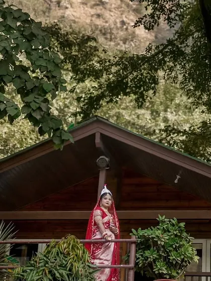 Another stunning portrait of our Bengali bride, set against a backdrop of lush trees and mountains. This shot emphasizes the beauty of a destination wedding and the elegance of traditional bridal wear.