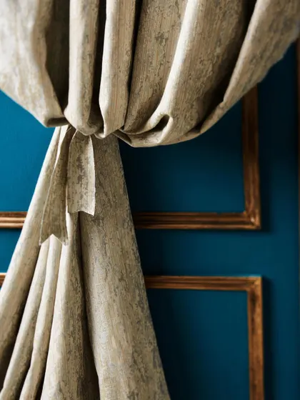 A close-up of a textured curtain against a bold blue wall with gold trim. This shot highlights the luxurious feel of the fabric and creates a rich, jewel-toned color story.