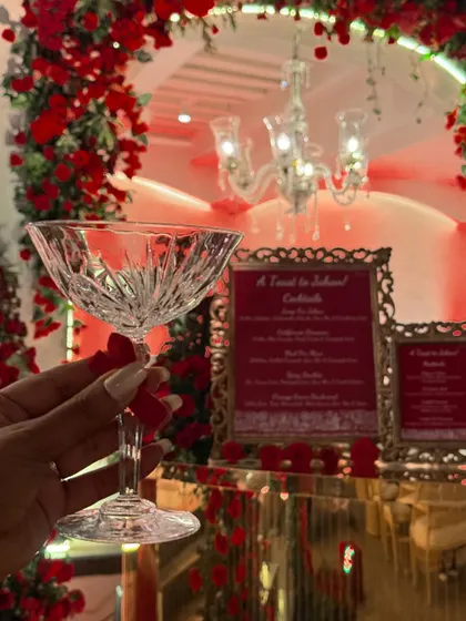 A guest's perspective, holding a beautiful crystal coupe glass against the backdrop of our elegantly decorated bar. This image captures the sophisticated and personal experience we aim to create at every event.