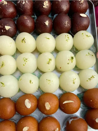 A tray showcasing some of my most popular sweets. You can see rows of spongy white Rasgullas, light brown Gulab Jamuns, and the richer, darker Kala Jamuns, all freshly prepared and ready to be enjoyed.