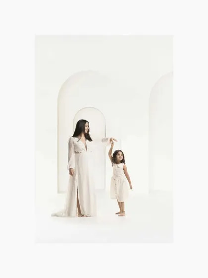 Guided by love, a mother gently holds her daughter's hand in a dance-like pose. The architectural arches in the white studio add a touch of elegance to this portrait of a mother's influence.