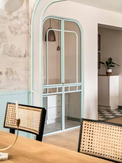 An arched metal and glass partition in a soft duck egg blue separates the dining and living areas in the Aqua Home. This custom element adds architectural interest while maintaining an open feel.