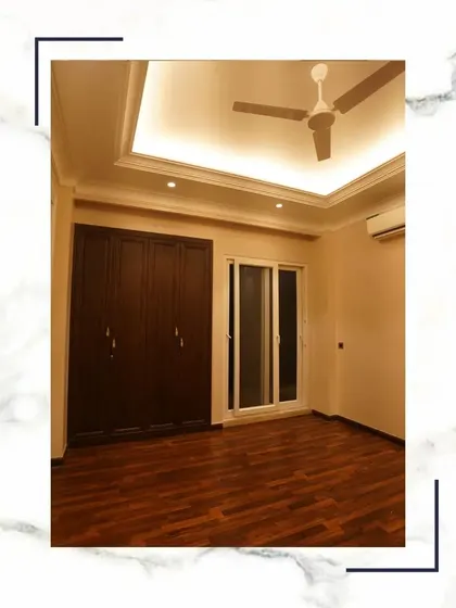 We build bespoke luxury. This bedroom features warm wooden flooring, a clean false ceiling design, and a large built-in wardrobe, offering a blend of style and functionality.