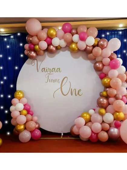 A chic first birthday celebration for Vairaa, using a beautiful rose gold, pink, and gold balloon garland on a custom circular backdrop. The large foil '1' balloon adds the perfect touch.