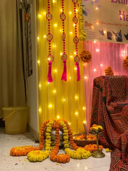 A detail shot of the Haldi ceremony decor, showing traditional elements like marigold garlands, a brass 'urli' bowl, and decorative hangings against a backdrop of fairy lights.