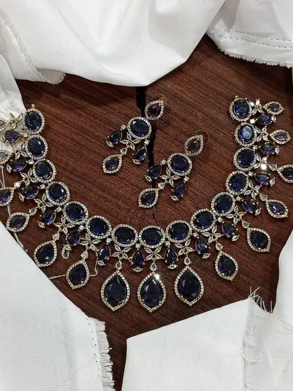 A stunning AD necklace set laid out to show its full design. This piece is available in multiple vibrant colors like ruby red, emerald green, pastel blue, and sapphire blue, featuring teardrop-shaped stones.