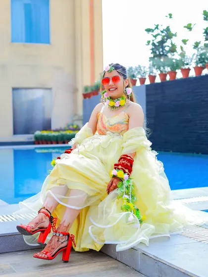 A quirky and fun bridal portrait by the pool during the Haldi ceremony. The bride's modern outfit and red heels add a unique touch to the traditional celebration.