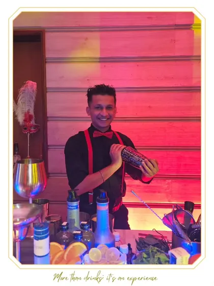 A smiling bartender in a red bow tie and suspenders shakes a cocktail. This image captures the fun, stylish, and approachable energy our team brings to weddings and parties.