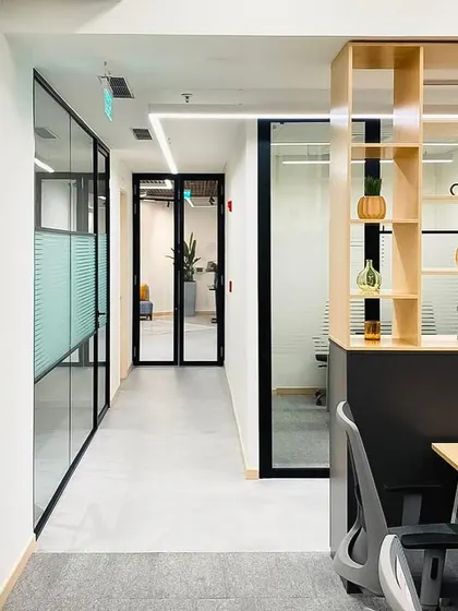 A corridor in the DLF hospitality office, showing the clean lines and material palette. The combination of glass partitions, wood shelving, and neutral flooring creates a bright and modern corporate interior.