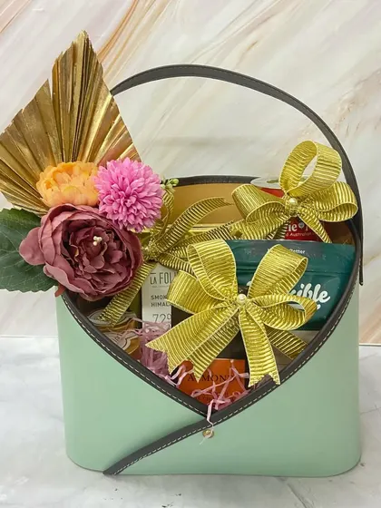 A chic and modern Mother's Day surprise basket. This mint green envelope-style container is filled with gourmet goodies and adorned with a beautiful floral arrangement.