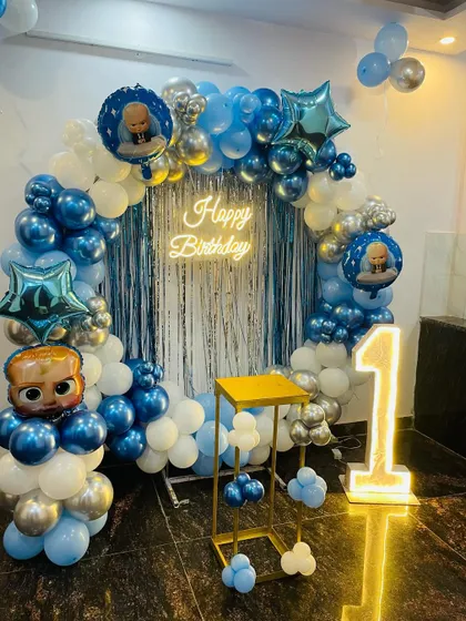 A classic Boss Baby first birthday setup. This circular balloon arch in blue, white, and silver chrome is perfect for photos, complete with a neon sign and light-up number.