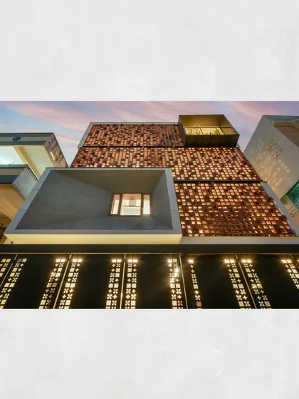 The Kamala Residence at dusk, when the terracotta jaali facade transforms into a lantern. The interplay of light from within highlights the intricate pattern, creating a warm and inviting presence.