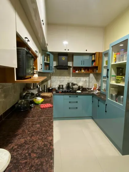 A completed kitchen project with teal-colored cabinets, a granite countertop, and practical storage solutions, demonstrating a vibrant and functional design.