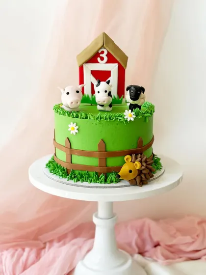 Old MacDonald had a farm, and it looked something like this. This cake features a red barn, a fence, and cute fondant figures of a pig, cow, and sheep on a field of green buttercream grass.