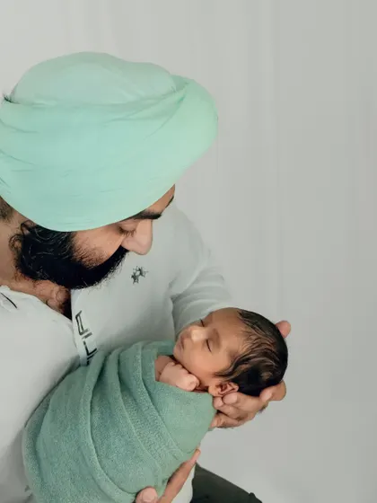 A father holds his newborn, wrapped in a soft green swaddle that complements his turban. The image is a beautiful blend of modern fatherhood and cultural identity.